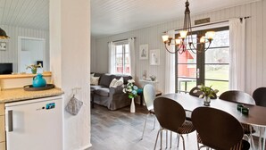 Eine moderne Küche mit einem weißen Kühlschrank, einem Essbereich mit Tisch und Stühlen, einer Couch und einem Fenster mit Vorhängen.