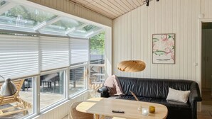 Ein modernes Wohnzimmer mit einem schwarzen Ledersofa, einem Holztisch und einem großen Fenster mit Jalousien.