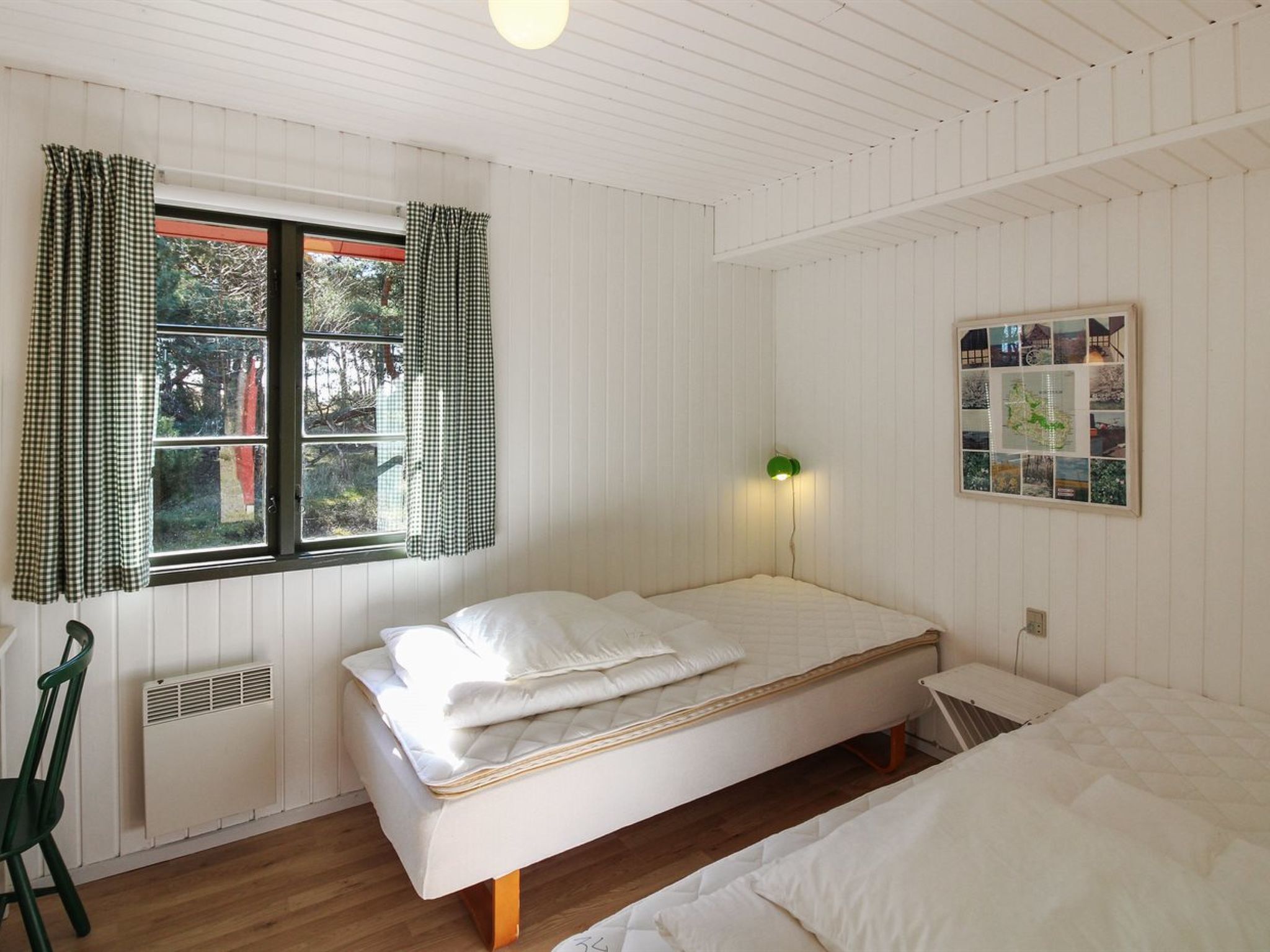 Ein Zimmer mit einem Einzelbett, einem Fenster, einer an der Wand befestigten Karte und einer Heizung.