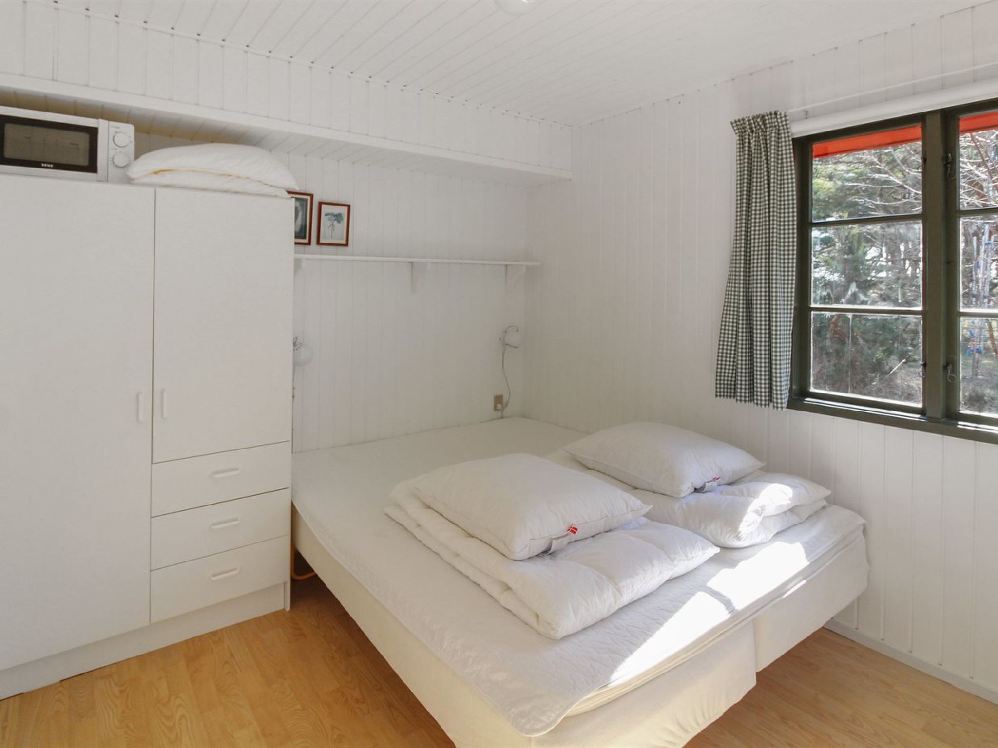 A bedroom with a bed, white wardrobe, and a window with curtains.