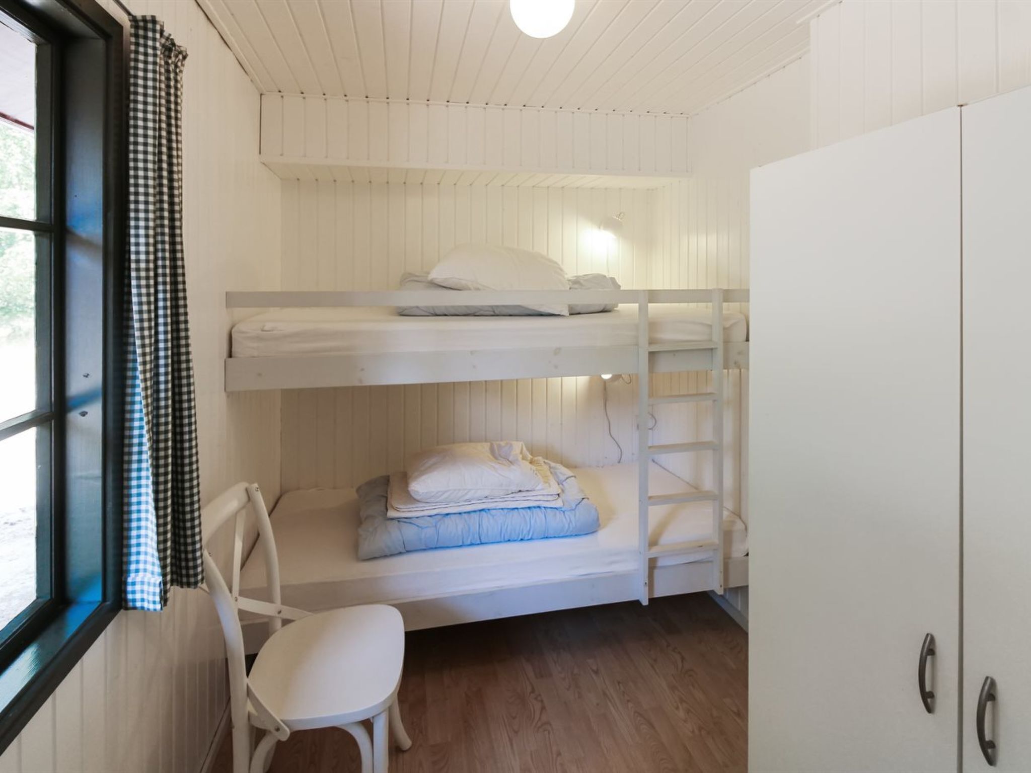 A bunk bed room with a window, a chair, and a wardrobe.