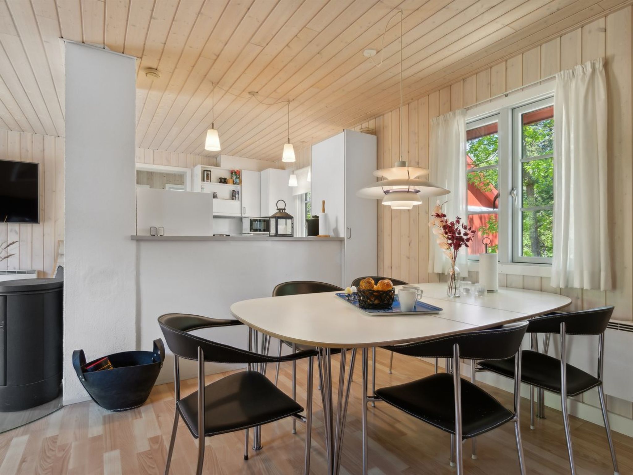 A modern kitchen with white cabinets, a dining table with black chairs, and a window with curtains.