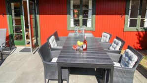 En rød bygning med tegltag og en terrasse med bord og stole.