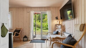 Et hyggeligt værelse med trævægge og trægulv, en sofa, et bord og et fjernsyn hængt på væggen.