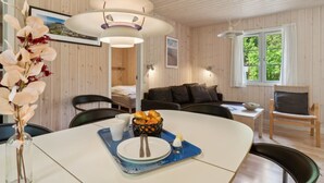 Et moderne, velbelyst rum med træloft, et spisebord dækket med tallerkener, en vase med blomster og en kurv med croissanter.
