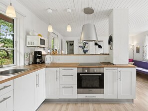 Eine moderne Küche mit weißen Schränken, einem Bosch-Backofen, Pendelleuchten und Blick ins Freie.