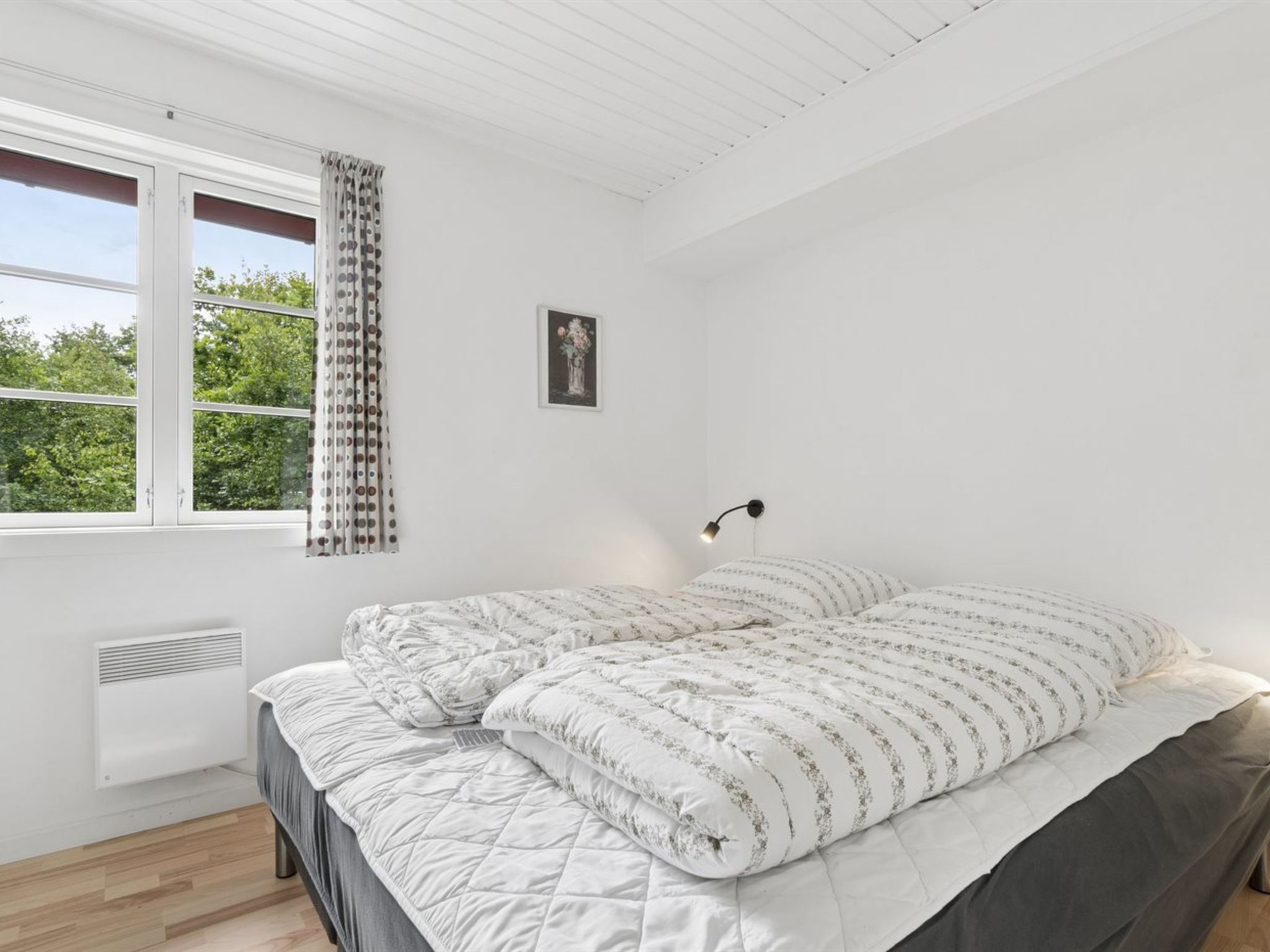 A bedroom with a bed, a window with curtains, a radiator, and a wall-mounted light fixture.