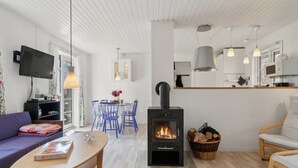 A modern living room with a wood-burning stove, a dining area with blue chairs, a sofa, and a television. - "Georg" - 300m from the sea by Interhome (Nexø)