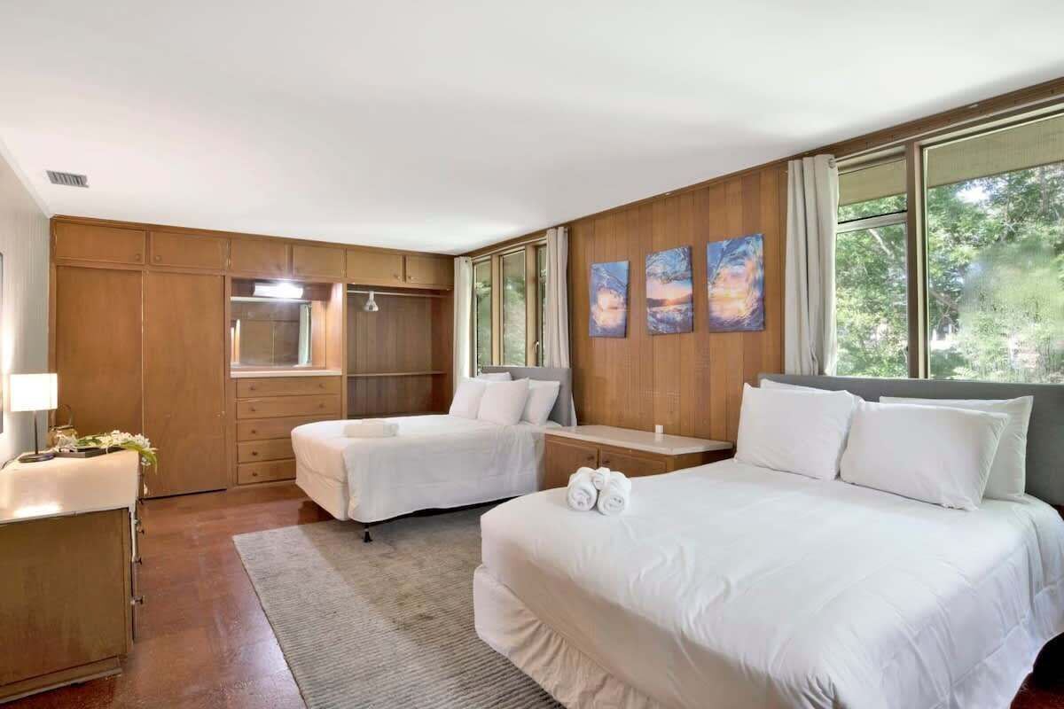 A bedroom with two beds, wooden wardrobe, and large windows.