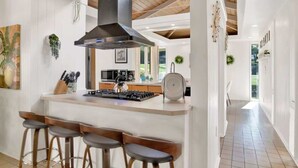 A modern kitchen with a central island, bar stools, a stove, and a large range hood. - Midcentury Modern -Hot Tub - Retro Retreat (Mobile)