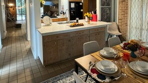 A spacious kitchen with a central island, a dining area with a table set for four, and a view of the adjacent living area. - Midcentury Modern -Hot Tub - Retro Retreat (Mobile)