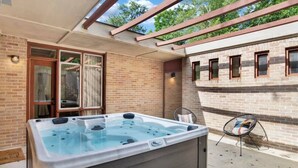 A hot tub in a covered outdoor area with a brick wall and windows. - Midcentury Modern -Hot Tub - Retro Retreat (Mobile)