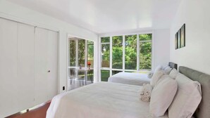 A bedroom with a large bed, a desk, and a view of greenery through the windows. - Midcentury Modern -Hot Tub - Retro Retreat (Mobile)
