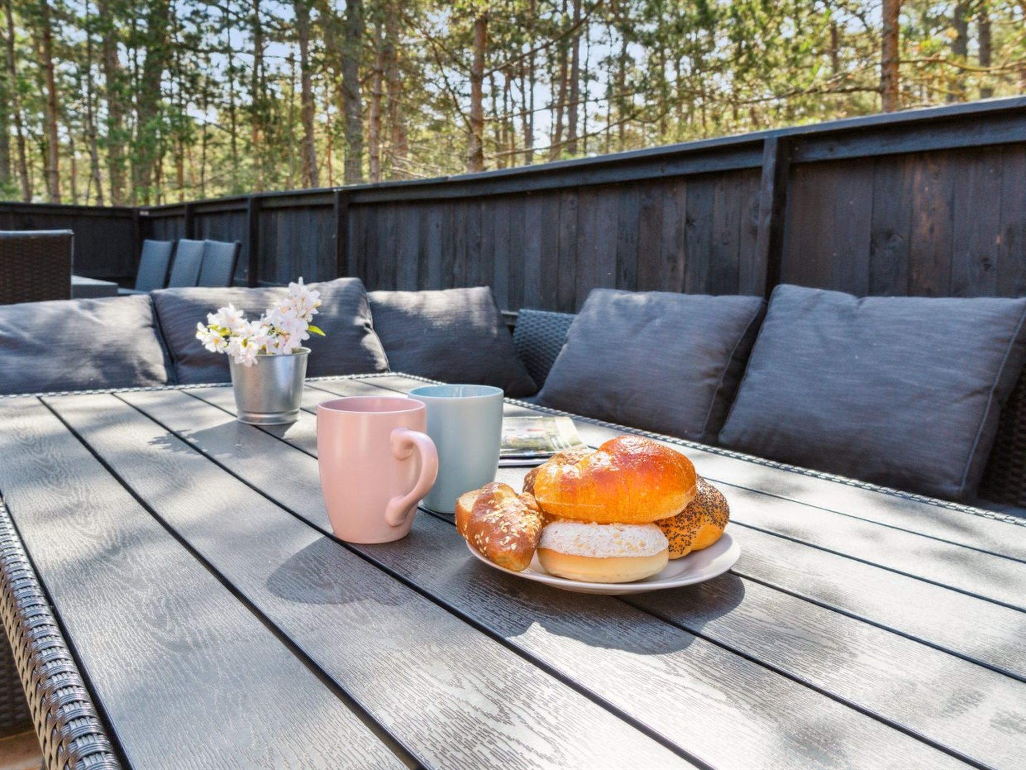 Puisesta pöydästä löytyy lautanen, jossa on leivonnaisia, kaksi mukia ja pieni kukkaruukku.