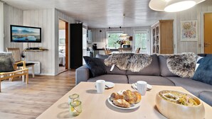 Ein modernes Wohnzimmer mit einer Couch, einem Couchtisch mit Gebäck und einem Fernseher im Hintergrund.