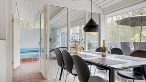 A dining area with a table, chairs, a hanging light fixture, and a view of an outdoor swimming pool. - "Dagi" - 300m from the sea by Interhome (Nexø)