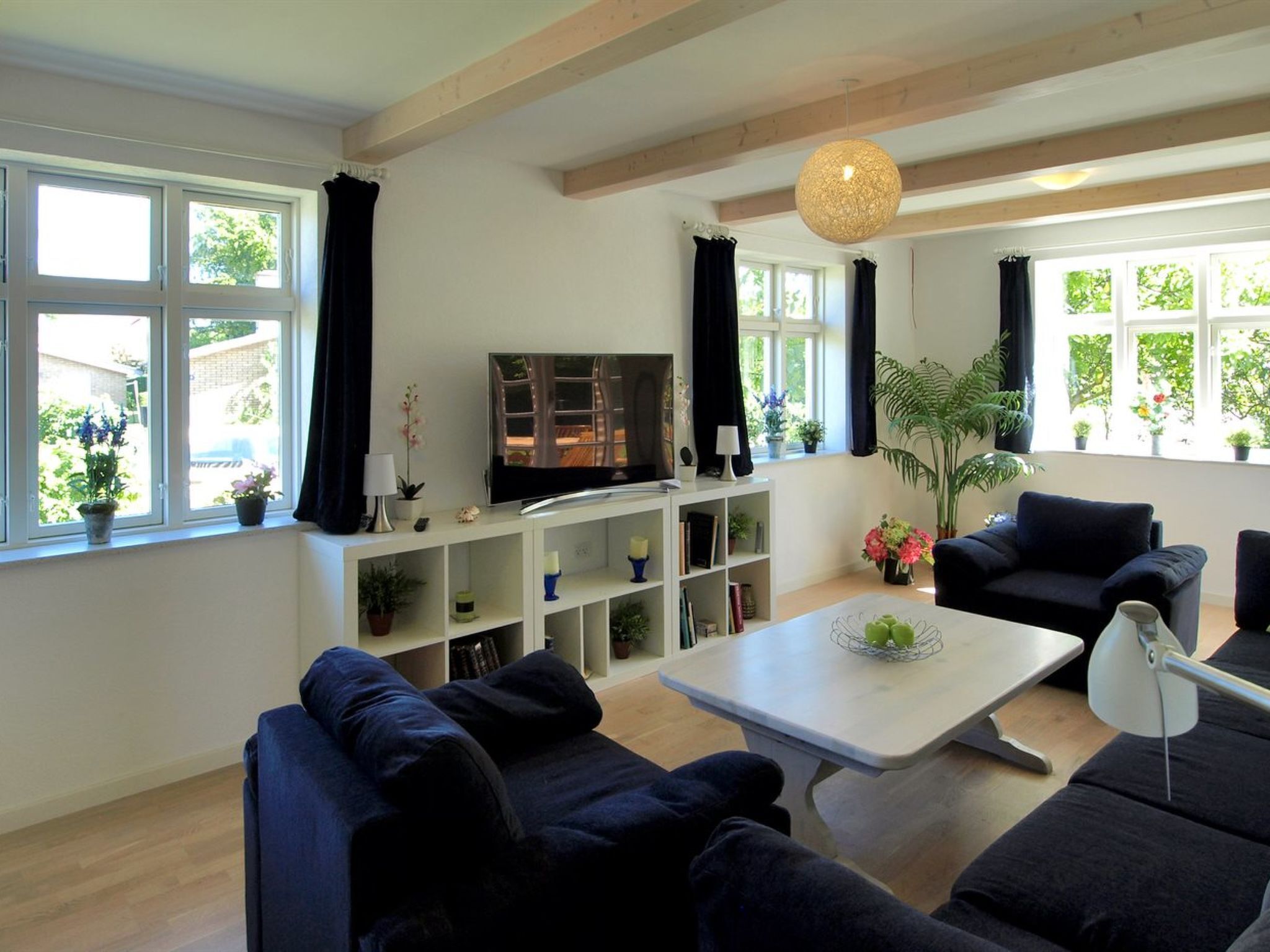 A modern living room with a flat-screen TV, dark sofas, a coffee table, and a bookshelf.