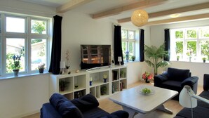 A modern living room with a flat-screen TV, dark sofas, a coffee table, and a bookshelf.