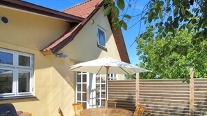 A patio with a round wooden table and chairs, a barbecue grill, and a white umbrella.