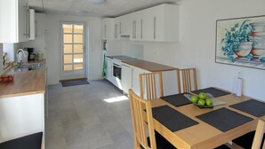 A modern kitchen with white cabinets, a wooden dining table with black placemats, and a painting of potted plants on the wall.