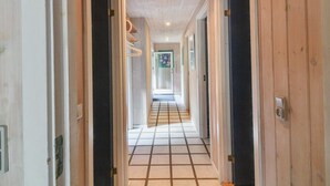 A hallway with wooden walls and a tiled floor, leading to a room with a bed and a window.