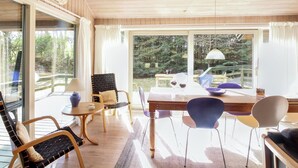 A room with a wooden ceiling, large windows, a dining table, and various chairs.