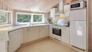 A kitchen with white cabinets, a microwave, a refrigerator, and a window overlooking greenery.