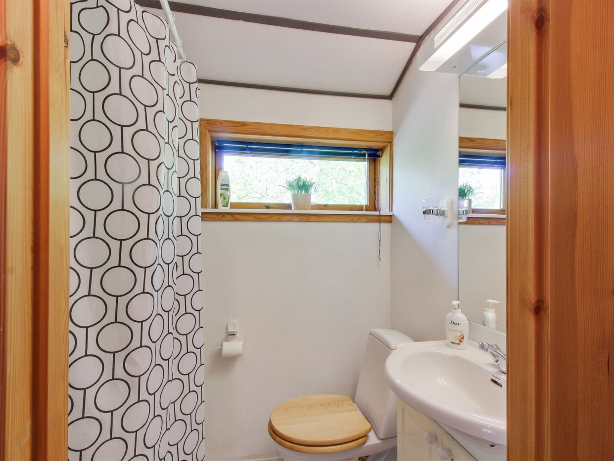 Ein kleines, kompaktes Badezimmer mit Toilette, Waschbecken und einem Fenster über der Toilette.