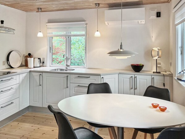 A modern kitchen with white cabinets, a round dining table, and pendant lighting.