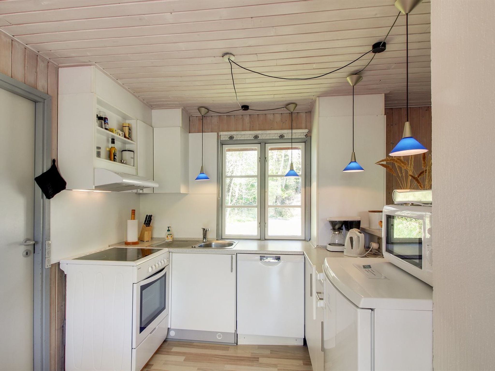 A compact kitchen with white cabinetry, a built-in oven, a sink, and a window with a view of greenery.