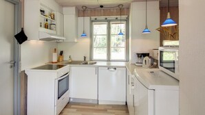 Ett kompakt kök med vita skåp, en inbyggd ugn, en diskho och ett fönster med utsikt över grönområden.