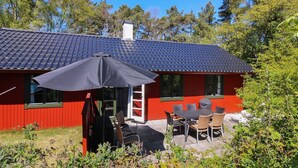 En röd byggnad med ett tak täckt av takpannor och en täckt uteplats med ett bord och stolar.