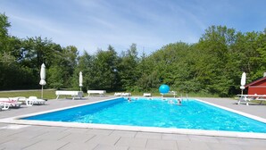 En rektangulär swimmingpool med ett kaklat poolområde, omgiven av solstolar och parasoller.