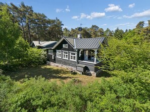 Mökki, jossa on kuisti, ja sen ympärillä on tiheää kasvillisuutta.