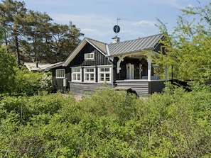 A black wooden house with a sloped roof, a satellite dish, and a porch.