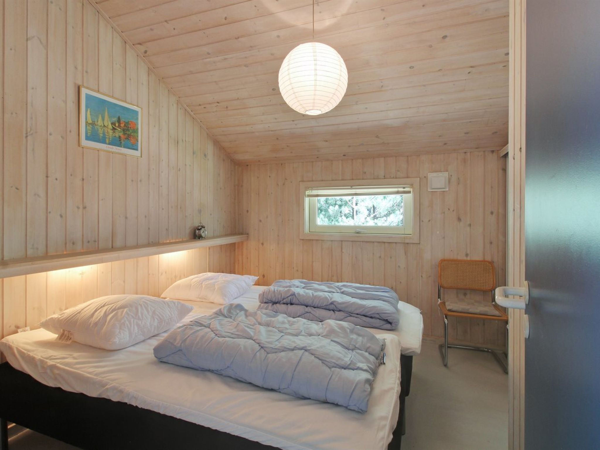 A cozy wooden room with two beds, a window with a view of trees, and a hanging light fixture.