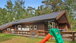 Eine Holzhütte mit einer Terrasse, Sitzgelegenheiten im Freien und einer Rutsche.