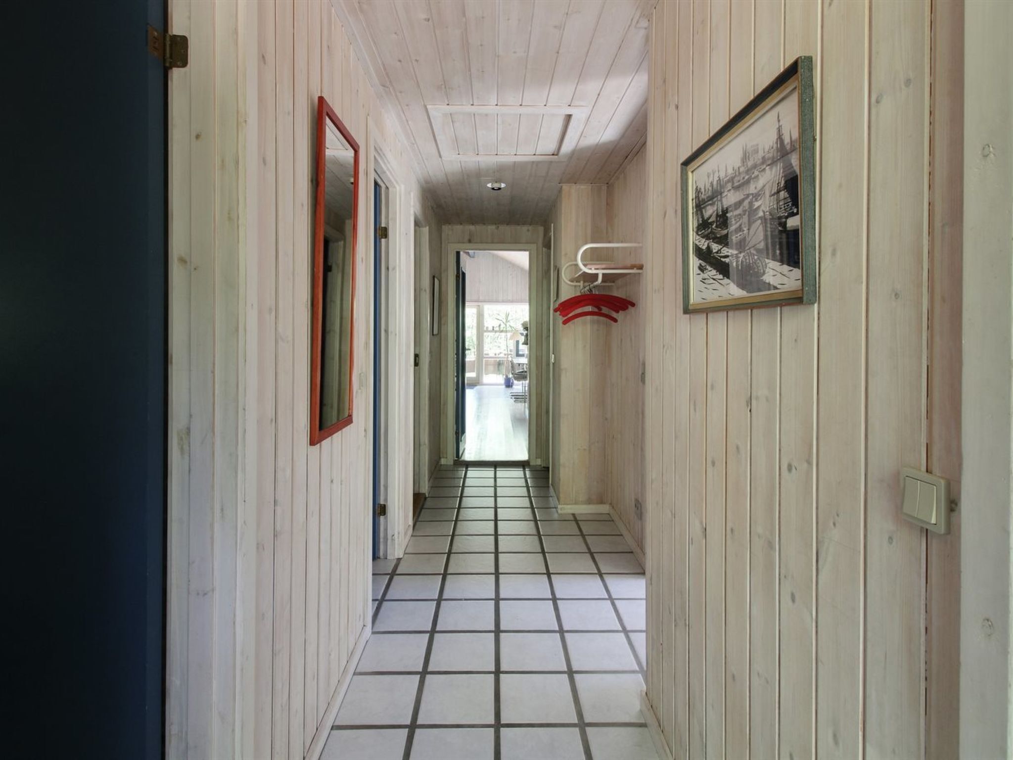 A narrow hallway with wooden walls, a tiled floor, and a door on the left.
