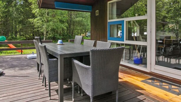 Ein überdachter Essbereich im Freien mit Tisch und Stühlen, großen Fenstern und einer Terrasse.