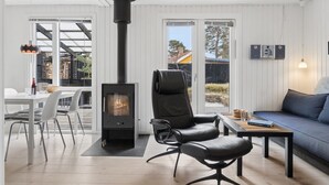 Ett modernt vardagsrum med en svart vedkamin, en soffa, ett matbord med stolar och ett stort fönster.