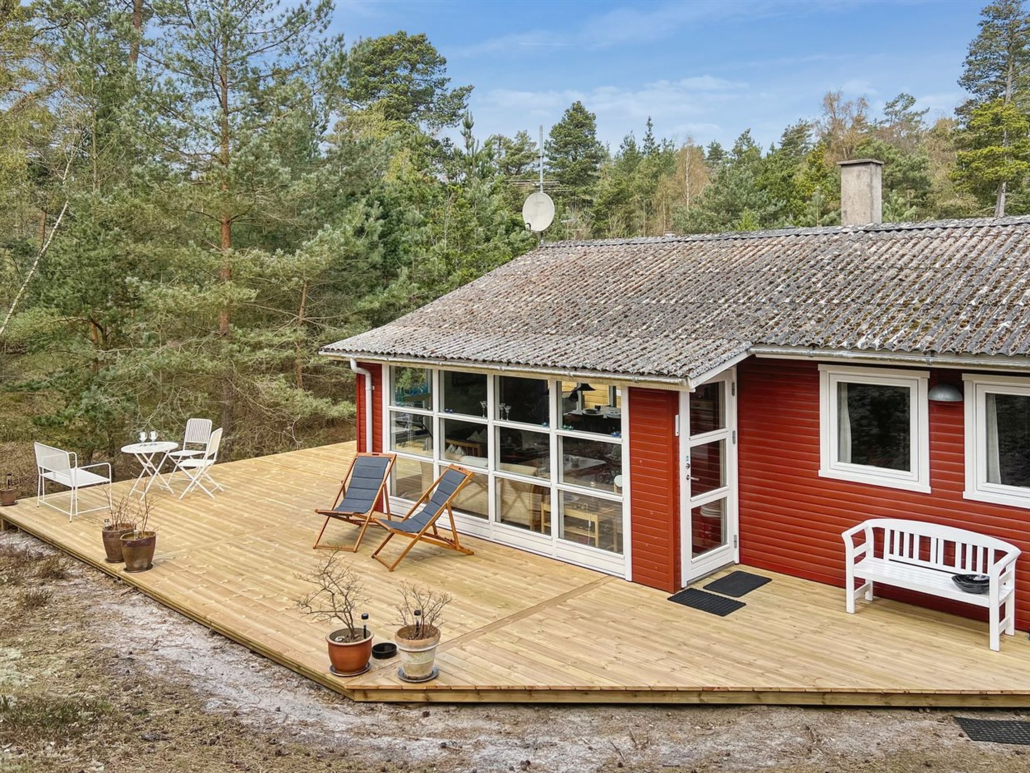 A wooden deck with outdoor furniture, a red building with large windows, and a forested backdrop.