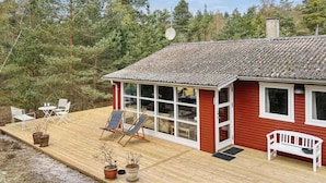 A wooden deck with outdoor furniture, a red building with large windows, and a forested backdrop. - "Kjeld" - 900m from the sea by Interhome (Nexø)