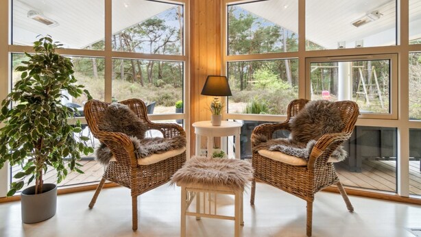 A room with large windows, two wicker chairs with fur throws, a small round table with a lamp, and a potted plant. - "Bergulv" - 75m from the sea by Interhome (Nexø)