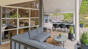 A covered outdoor seating area with a grey sofa, a round table, and black chairs. - "Bergulv" - 75m from the sea by Interhome (Nexø)