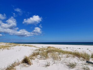 Ein Strand mit weißem Sand und vereinzelten Grashalmen.