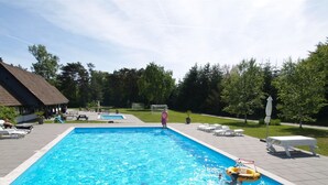 Una piscina rectangular con superficie de agua azul cristalina, rodeada por una terraza pavimentada con sillas de descanso y un pequeño edificio de techo inclinado.