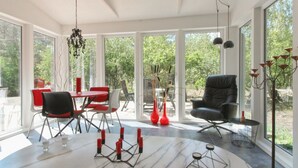 Una sala de estar moderna con un ventanal grande, un comedor con sillas rojas, un sillón de cuero negro y suelo de mármol.