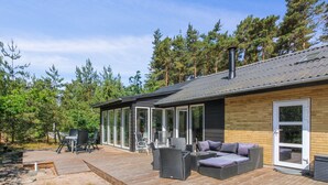 Una casa moderna con terraza, muebles de exterior y un amplio ventanal con vistas a un bosque.