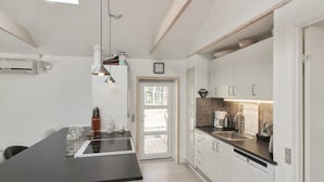 Cocina moderna con encimera negra, armarios blancos y horno integrado. Hay una ventana sobre el fregadero y un reloj en la pared.