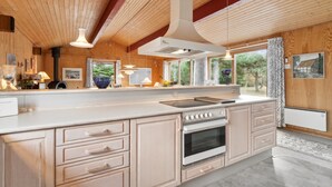 A modern kitchen with wooden beams, a large island with a built-in oven, and a view of the outdoors. - "Nada" - 200m from the sea by Interhome (Aakirkeby)